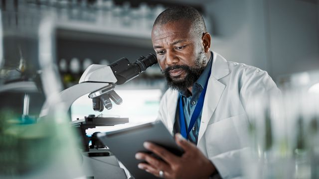 A scientist in a lab coat, sitting in front of a microscope. 