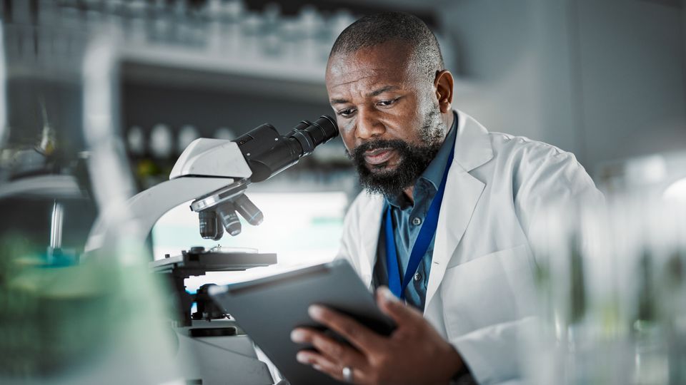 A scientist in a lab coat, sitting in front of a microscope.