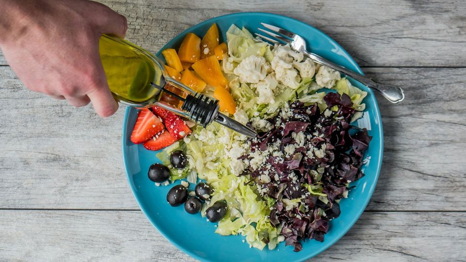 A person drizzles oil over a salad.