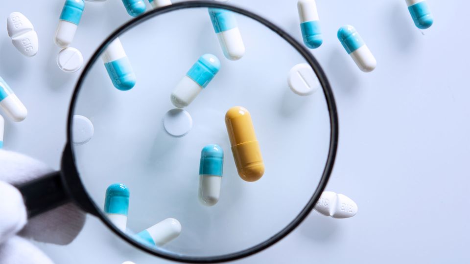 Magnifying glass focused on a yellow drug capsule amongst blue and white capsules.