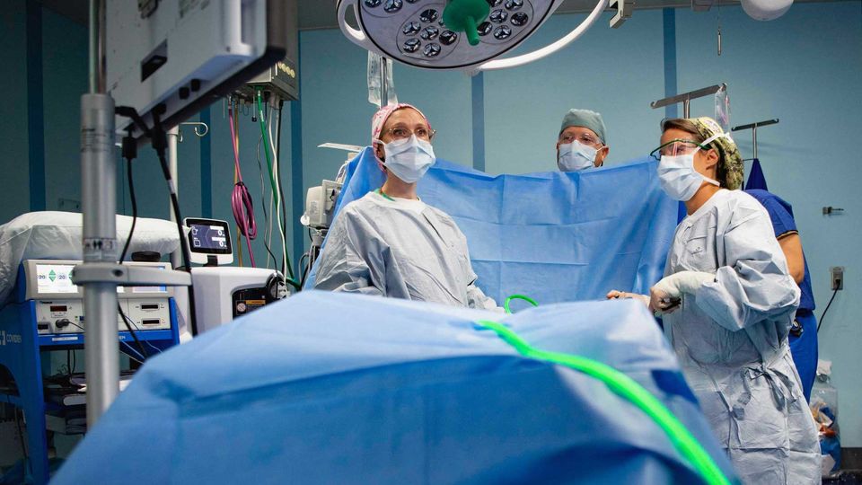 An anesthesiologist monitoring a patient in a surgical theatre during a procedure with other medical professionals.