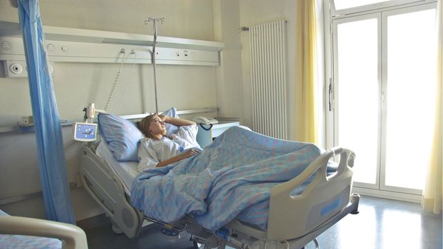 A woman lies in a hospital bed, gazing out of the window. 