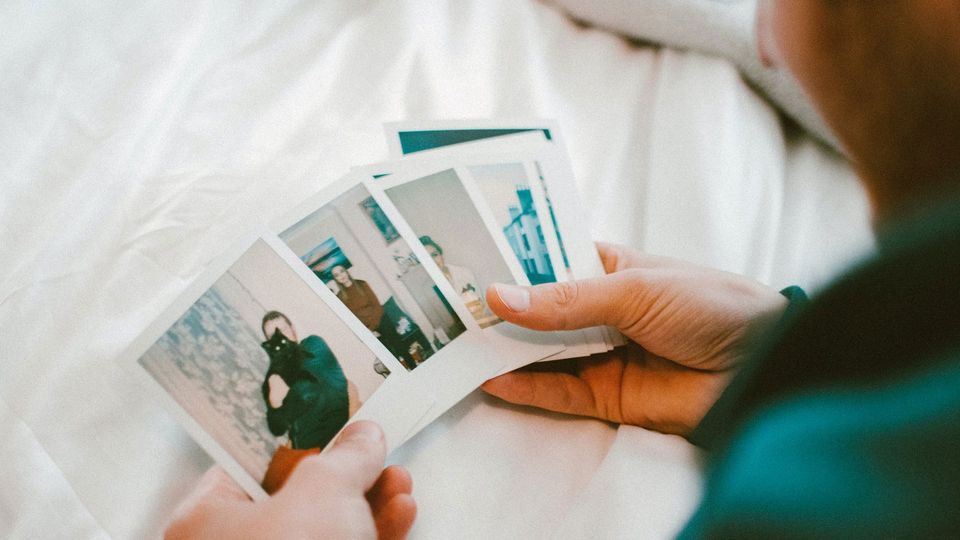 A person holds polaroid photos, symbolizing memory and forgetting.