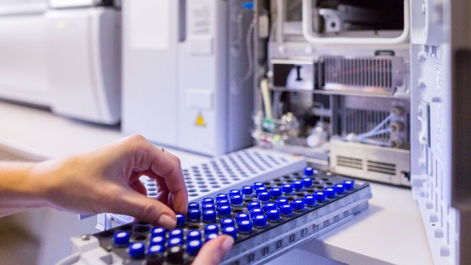 Scientist loading sample vials into a mass spectrometer for analytical testing in a lab.