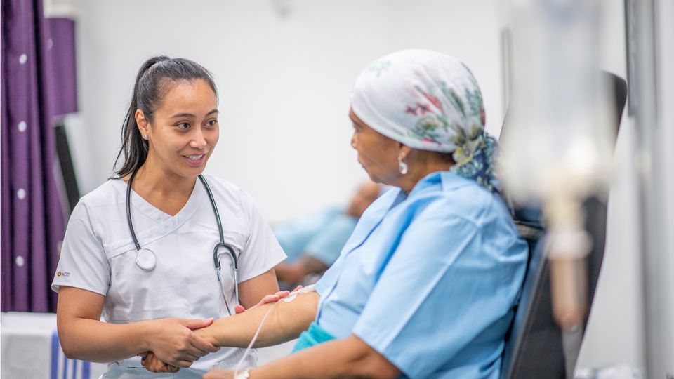 A female cancer patient receiving an IV talking to a female doctor.