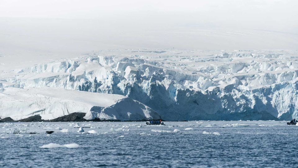 Snow-covered Antarctic mountains reflected in a calm, icy lake under a clear sky.