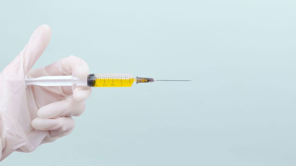 A gloved hand holds a syringe filled with yellow liquid, illustrating how nanobody treatment could be administered like a vaccine.
