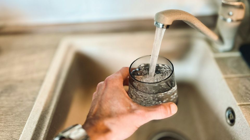 Hand fills a glass with water using a running tap