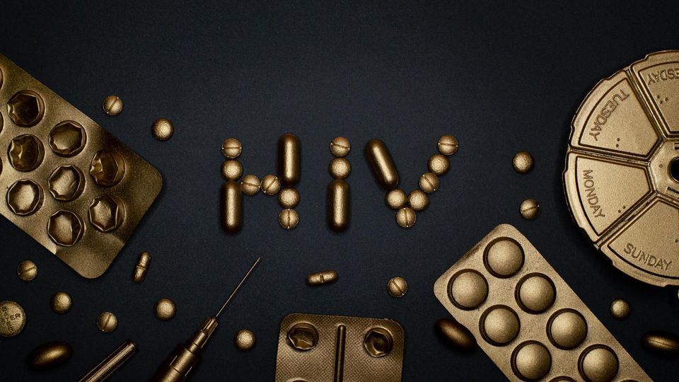 Blister packs and syringes surround gold colored oral medication spells out "HIV".