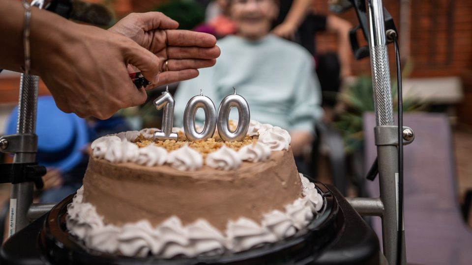Birthday cake with “100” candles celebrating a supercentenarian surrounded by family.
