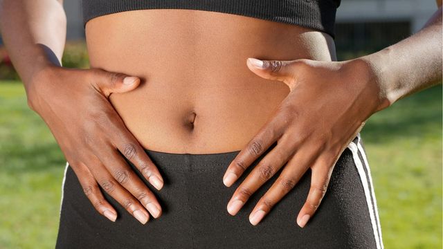Close-up of a woman’s hands on her stomach, symbolizing gut health and the gut microbiome. 