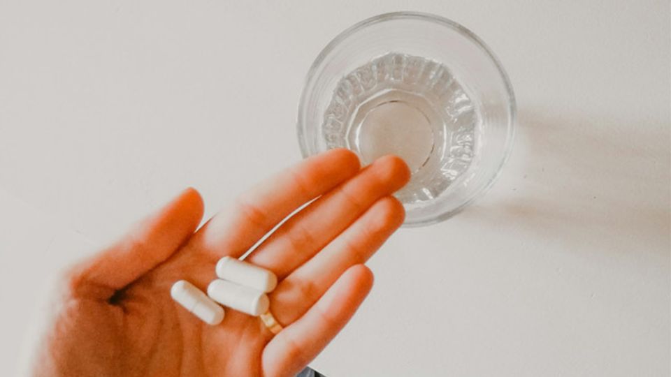 Hand holding probiotic capsules next to a glass of water, ready for supplementation.