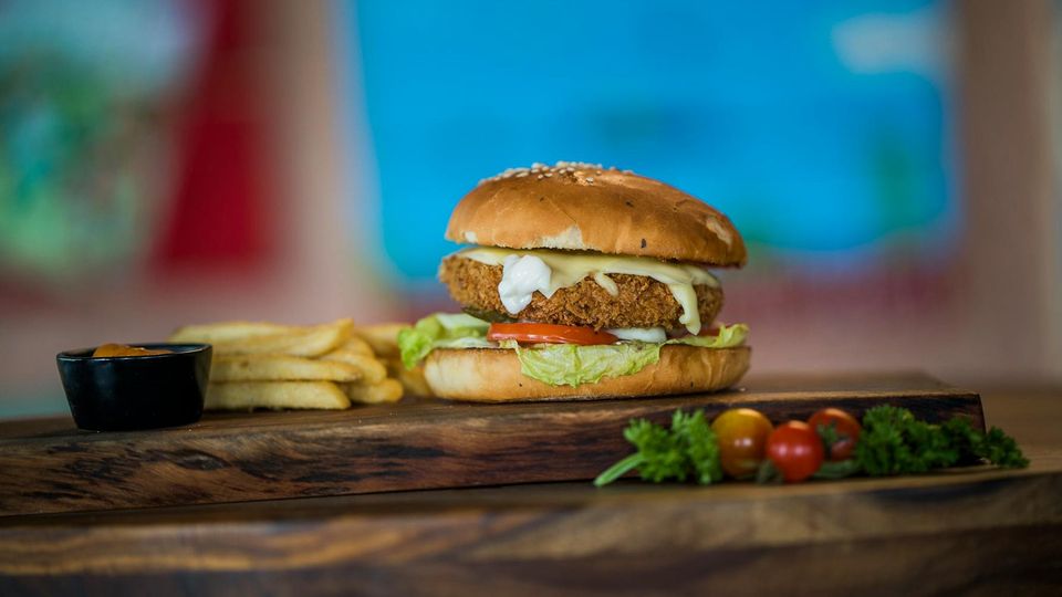 Ultra-processed veggie burger sits on a wooden board next to some fries and tomatoes