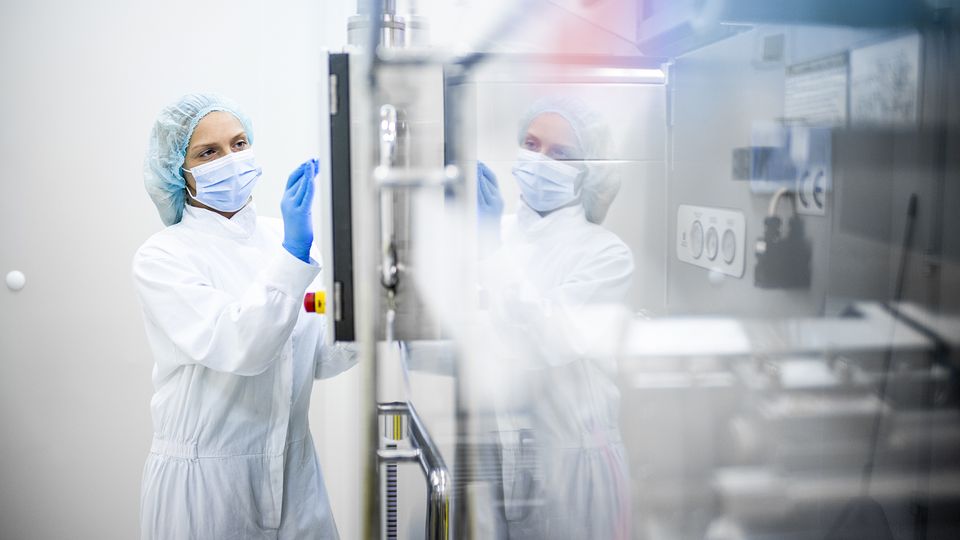 Scientist in sterile protective gear operating bioprocessing equipment in a cleanroom laboratory
