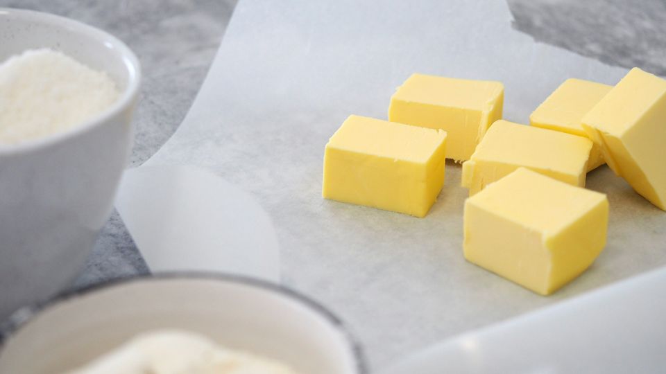 Cubes of margarine on baking paper, next two bowls of flour and sugar.