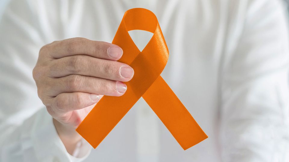 Hand holds an orange ribbon for multiple sclerosis awareness