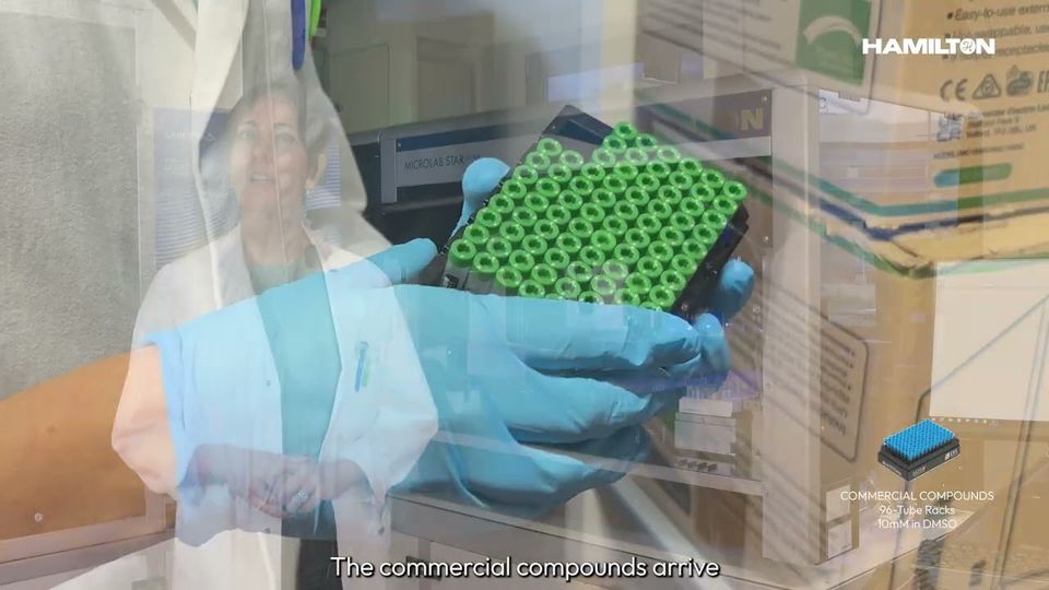 Scientist holding a rack of green-capped sample tubes in a lab, with Hamilton branding and lab equipment visible