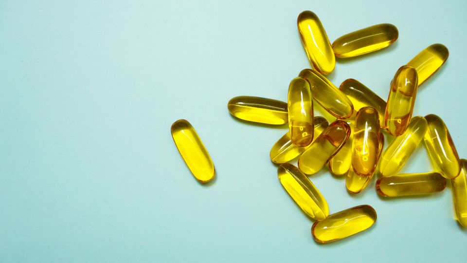 A pile of transparent yellow omega-3 supplement pills on a light blue background.