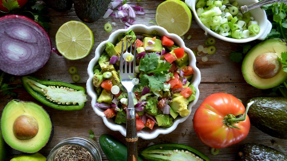 Fresh keto-friendly salad with avocado, tomato, lime and herbs on a rustic wooden table.