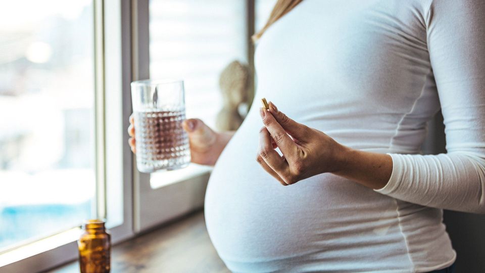 Pregnant woman taking vitamins with water.