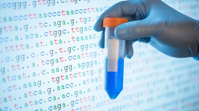 Gloved hand holding sample tube in front of DNA sequence data used in next-generation sequencing. 