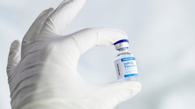Gloved hand holding a vial labeled mRNA COVID-19 vaccine, representing modern vaccine technology. 