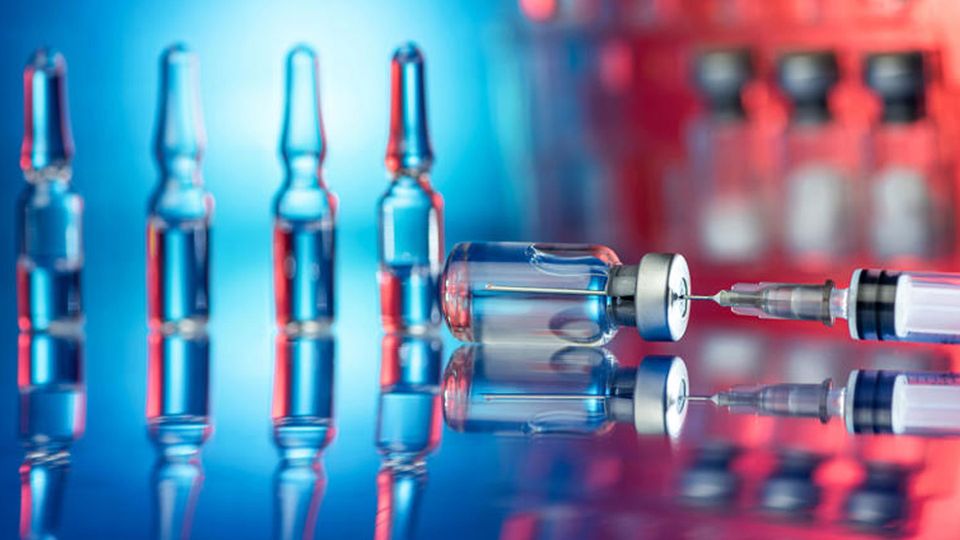 Needle and syringe in a drug vial in foreground, with other vials in background.