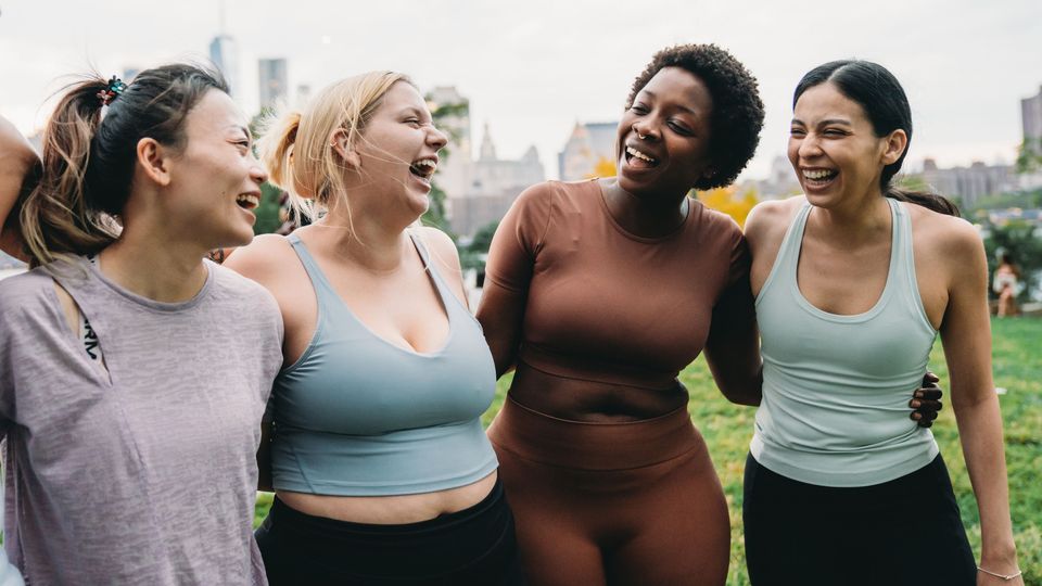 Group of diverse women in activewear laughing together outdoors, promoting women’s health and wellness.