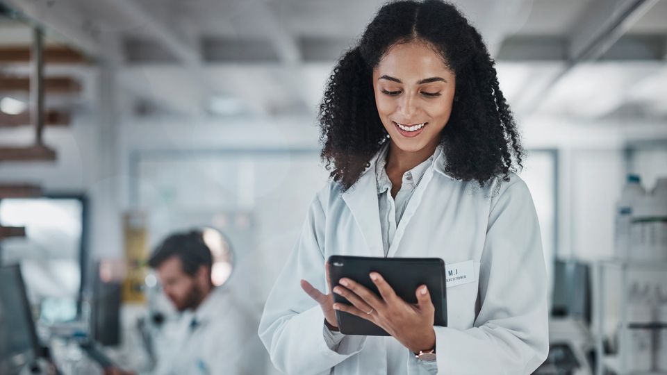 Female scientist in a lab coat using a digital tablet in a modern laboratory setting.