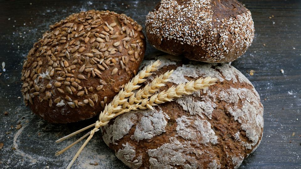 Three loaves of wholewheat bread, with a few pieces of wheat sprinkled on top.