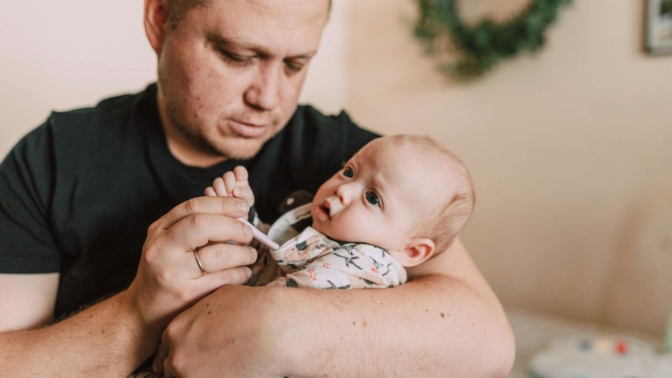 Concerned father checks baby's temperature with a thermometer, indicating possible infection.