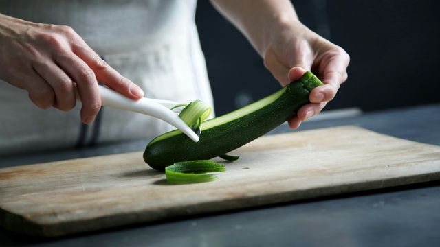 A chef peeling a zucchini on a wooden chopping board. 