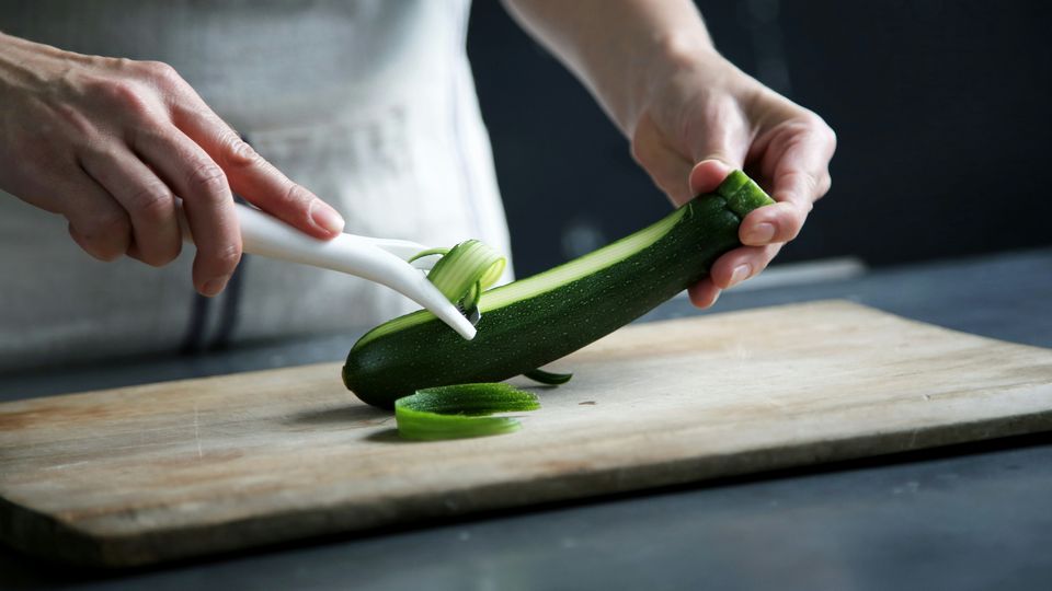 A chef peeling a zucchini on a wooden chopping board.