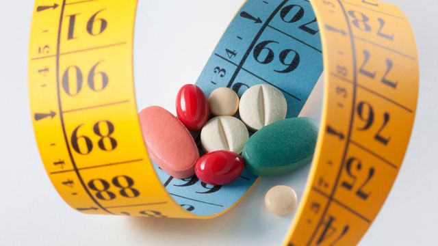 A collection of assorted pills surrounded by a curled measuring tape, symbolizing metabolic health. 
