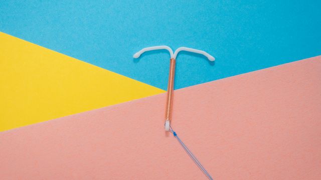 A T-shaped copper IUD, against a blue, yellow and pink triangular background. 