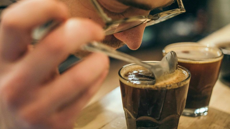 Person smelling freshly brewed coffee during aroma evaluation with a tasting spoon.