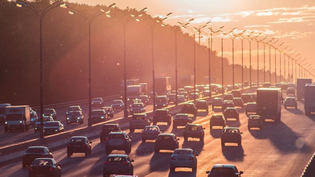 A large highway at sunset, with at least 5 lanes of cars heading in each direction. 