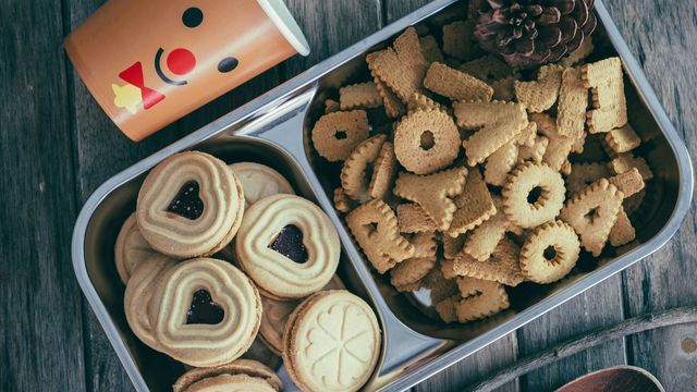 A metal tray carrying a selection of Christmas-themed cookies, with a reindeer-printed coffee cup next to it. 