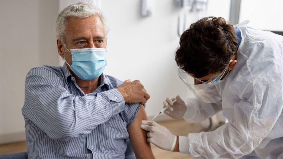 Older adult wearing face mask receiving vaccination.