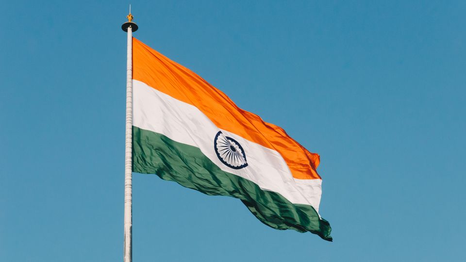 The flag of India, waving in the wind against a clear blue sky.