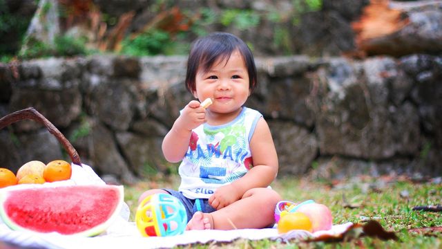 Smiling toddler eating fruit outdoors, illustrating the role of diet in shaping the toddler microbiome. 
