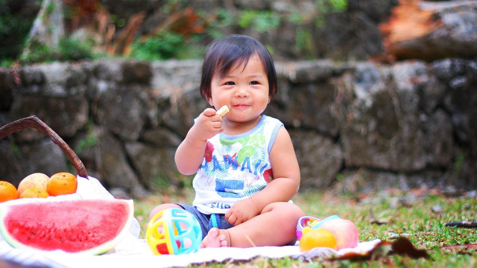 Smiling toddler eating fruit outdoors, illustrating the role of diet in shaping the toddler microbiome.