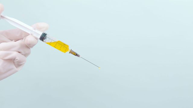 A syringe filled with yellow fluid, held by a gloved hand. 