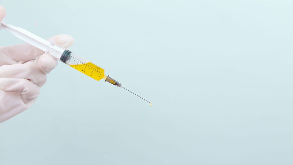 A syringe filled with yellow fluid, held by a gloved hand.