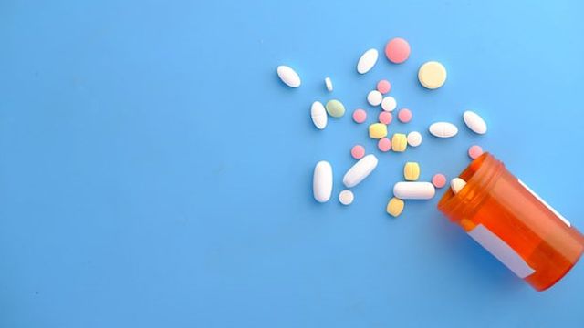 An orange prescription pill bottle spills multicolored pills onto a blue background. 