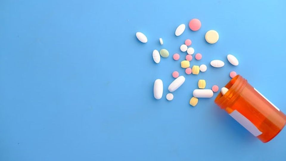 An orange prescription pill bottle spills multicolored pills onto a blue background.