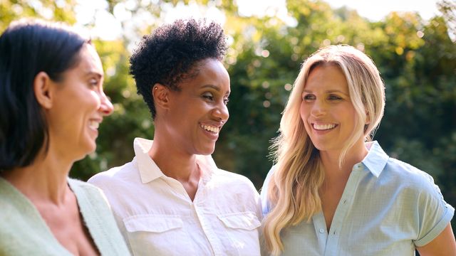 Three women smiling and talking outdoors, representing wellness and women's health. 