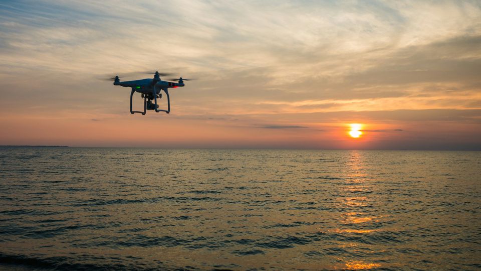 A drone flying by the shore at sunset.