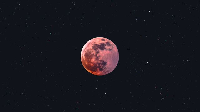 Reddish full moon in a starry night sky, captured during a lunar eclipse. 