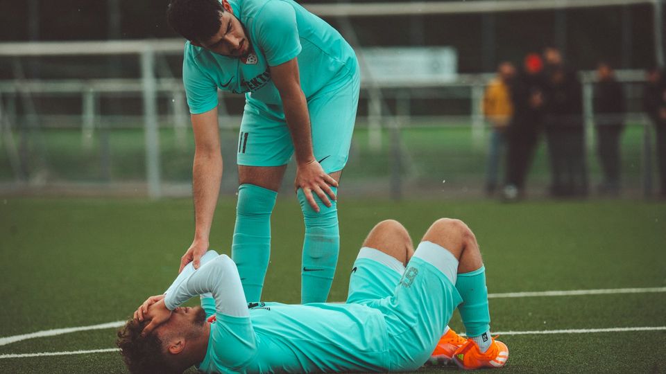 Soccer player lying on the field in pain, highlighting injury risks linked to CTE.